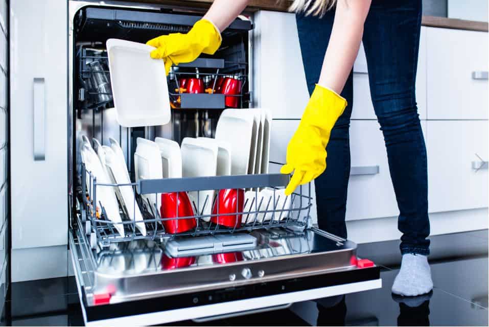 dishes being cleaned in a full dishwasher by a lady wearing yellow gloves