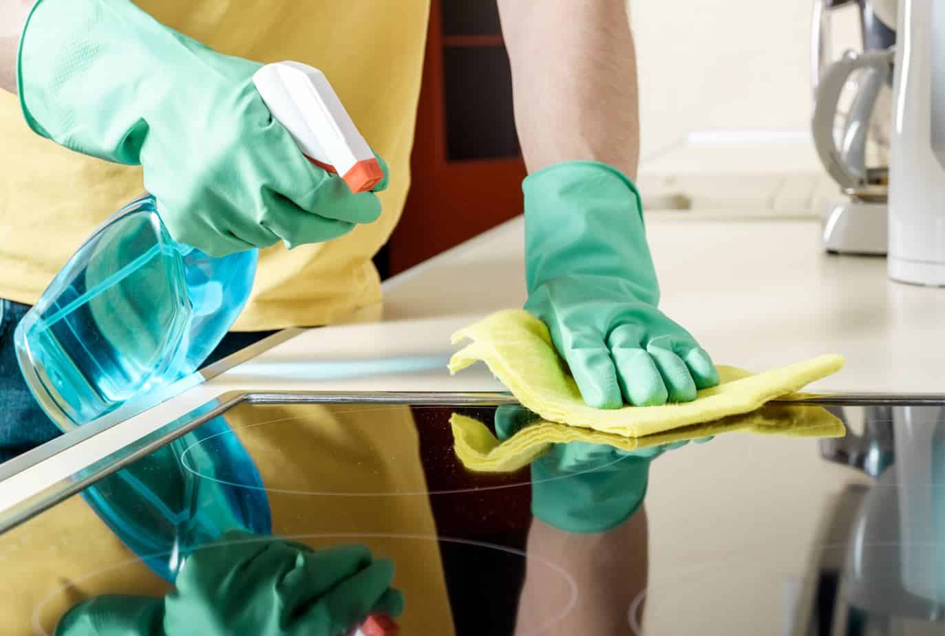 man wearing greeen gloves using a yellow microfibre cloth to clean an induction cooktop