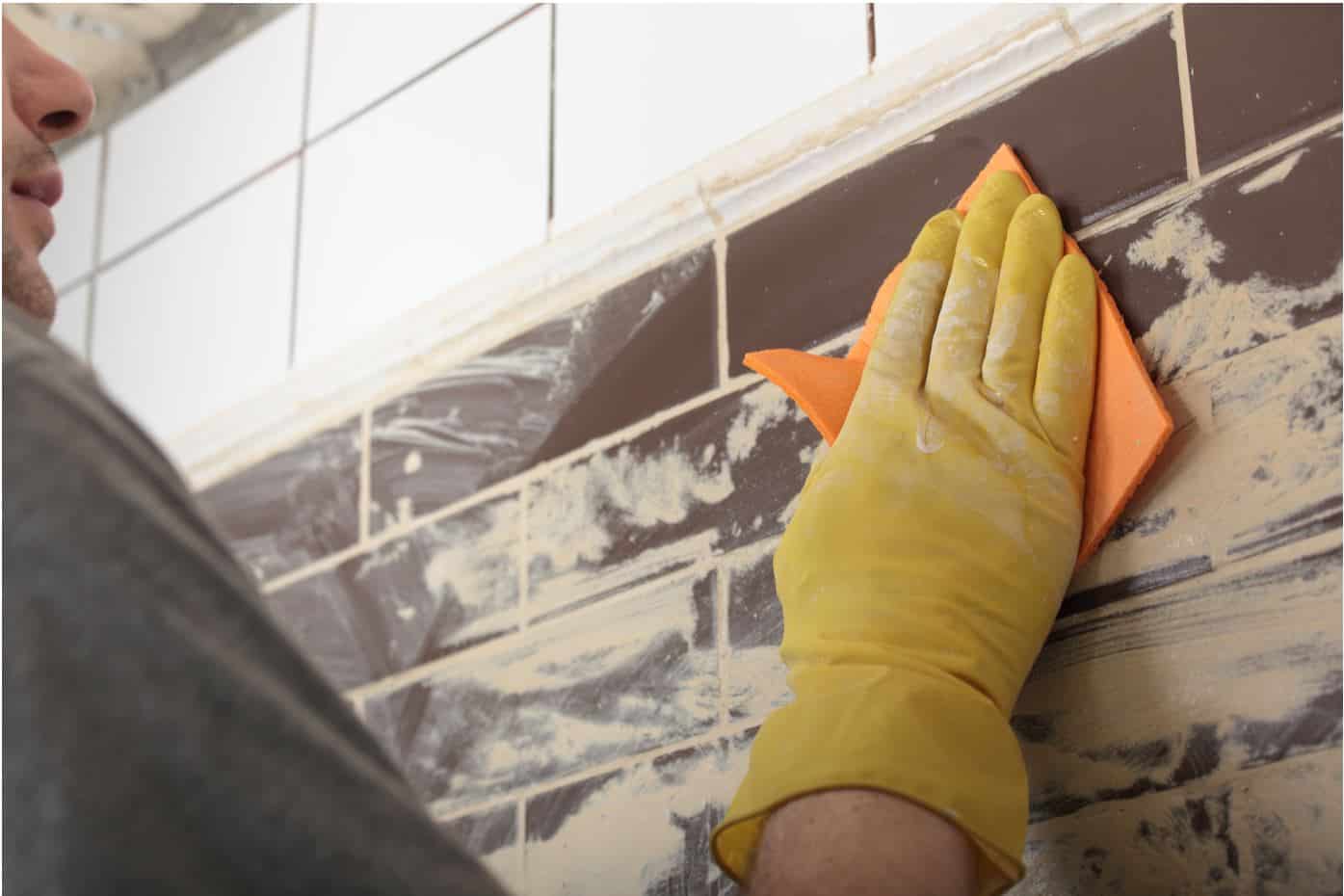 man wearing yellow gloves removing dirt from wall tiles