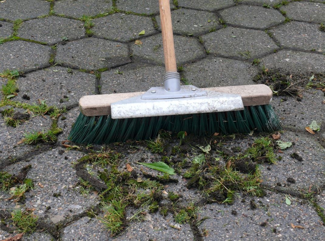 person using a hard bristled brush to clean a stone driveway