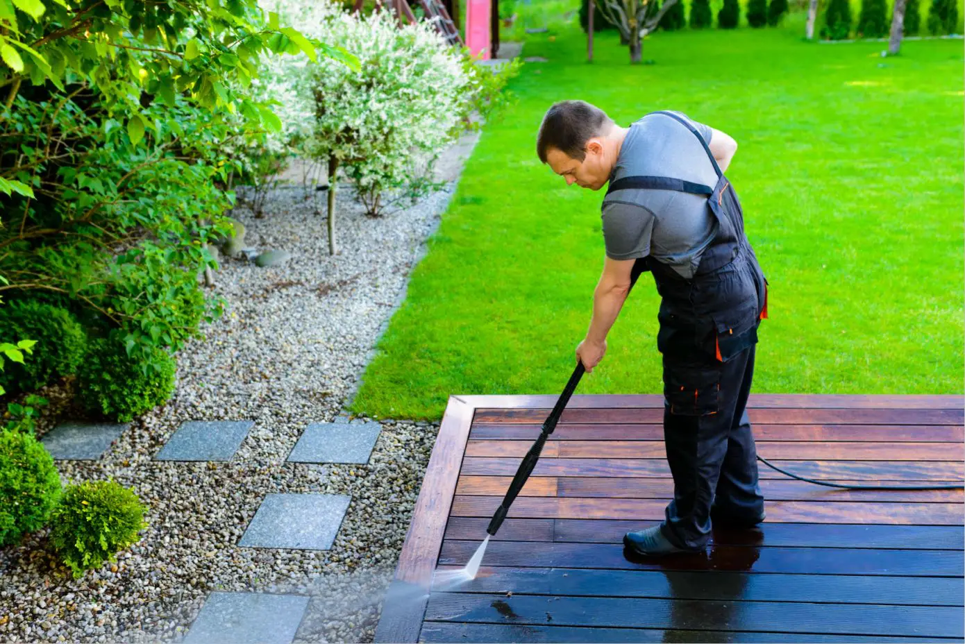 a man in dark overalls pressure cleaning a garden patio