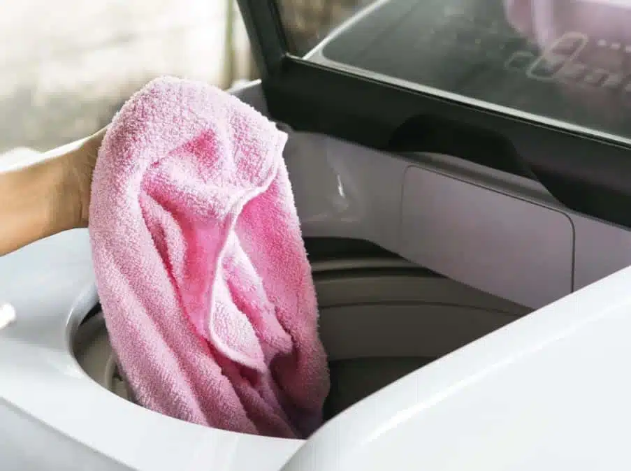 A person putting a pink towel into a top loader washing machine