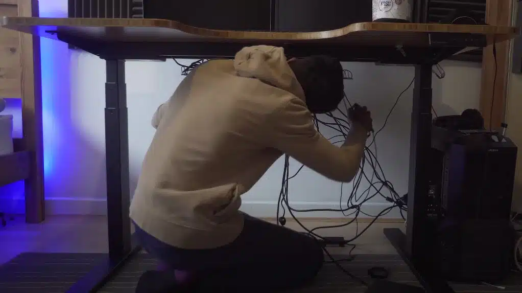 An office worker wearing a brown jumper doing cable management on his computer