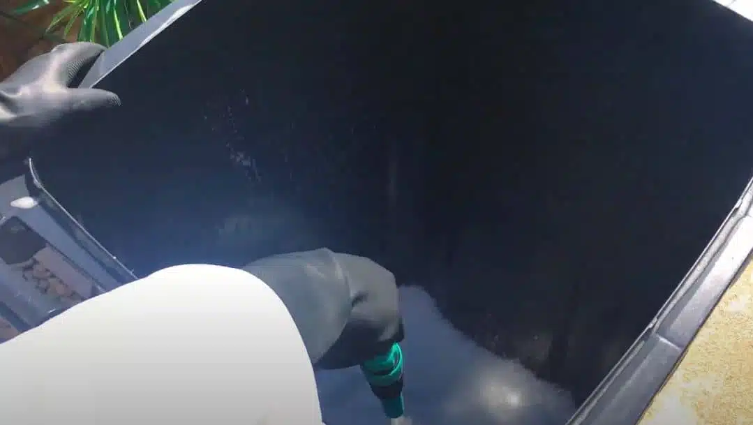 cleaning inside black wheelie bin with hose and soap