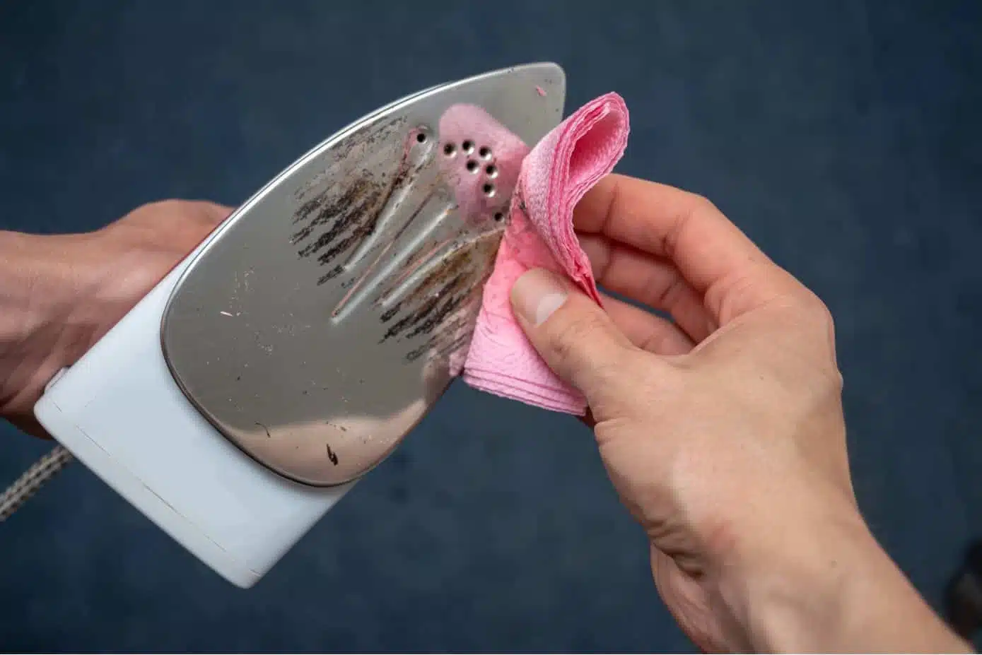 man cleaning dirty iron soleplate with pink cloth