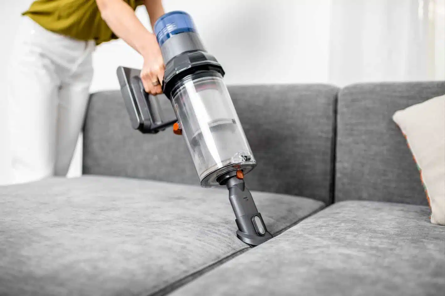 man cleaning grey couch cushions with a cordless vacuum and couch cleaning attachment