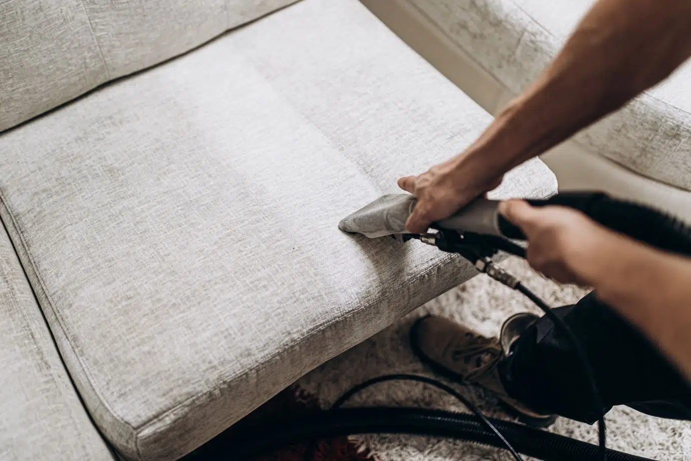 man using steam cleaning to deep clean a gray upholstered couch