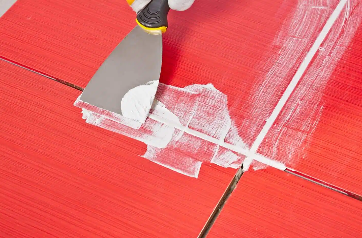 man using tool to work on grout in between red tile