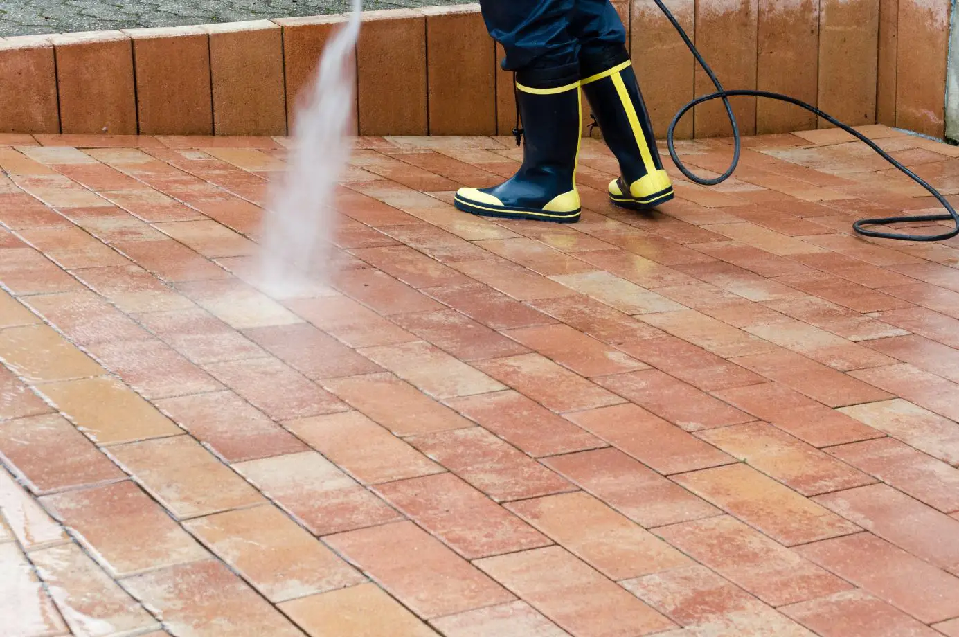 man wearing black boots pressure washing pavement tiles