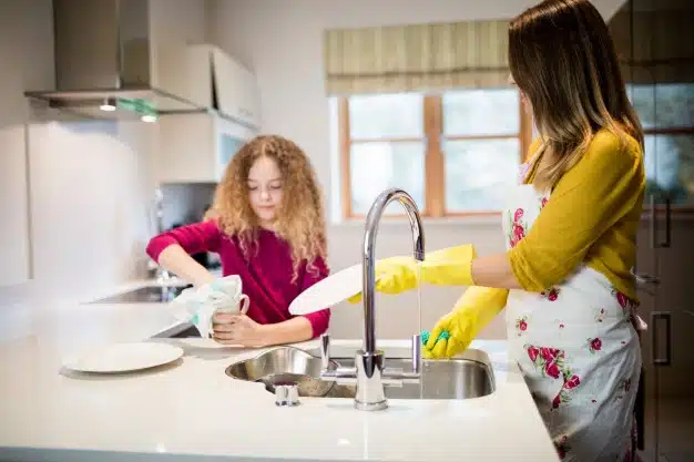 Mother assisting daughter washing plate kitchen