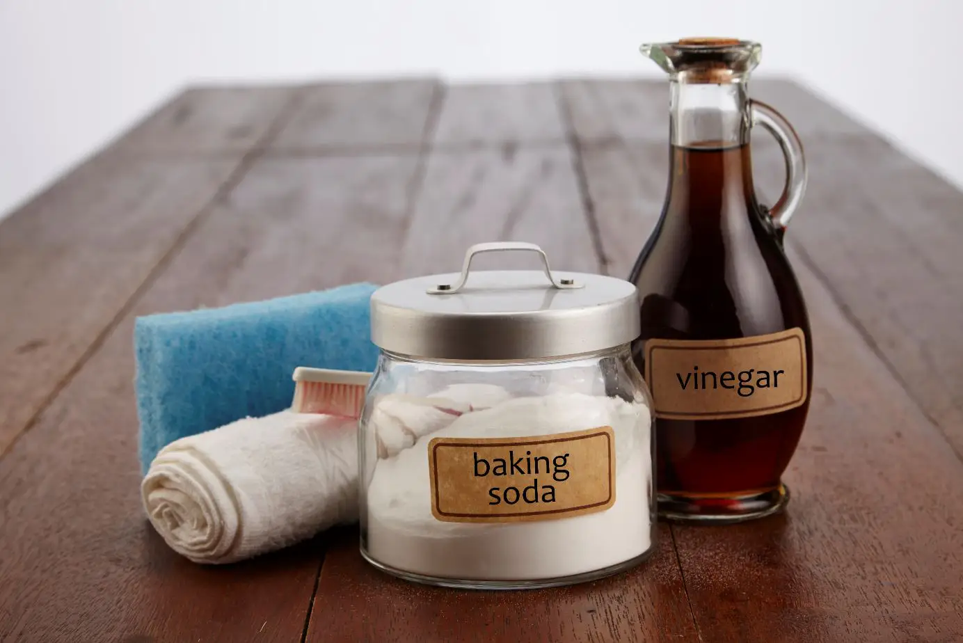 natural cleaning products labelled baking soda and vinegar on a wood table