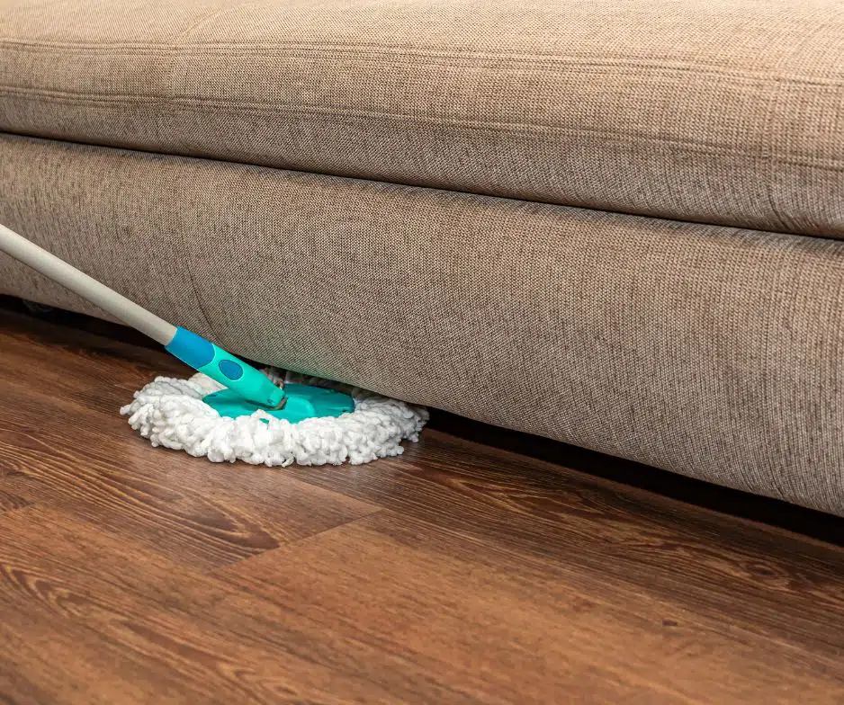 Person cleaning vinyl floor under fabric couch with a spin mop