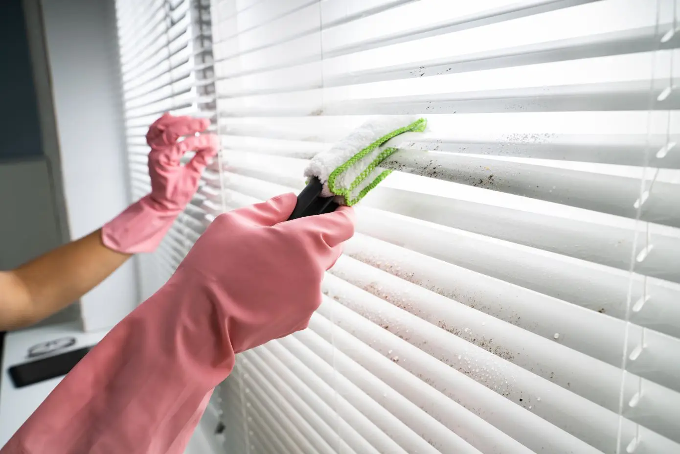 person cleaning window blinds with a dishwashing solution