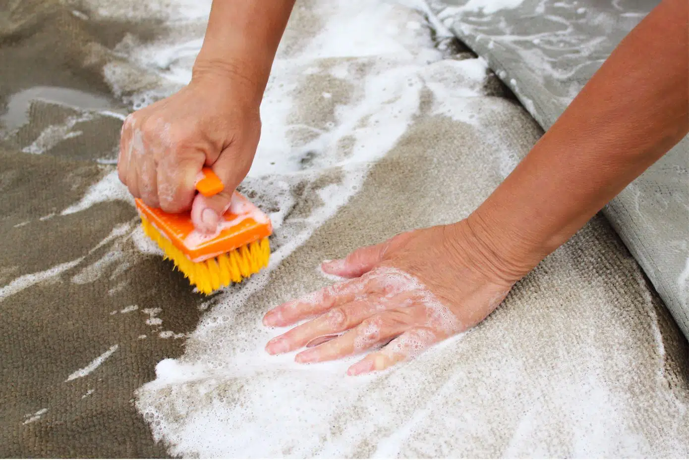 person hand washing carpet with a yellow hard bristled brush