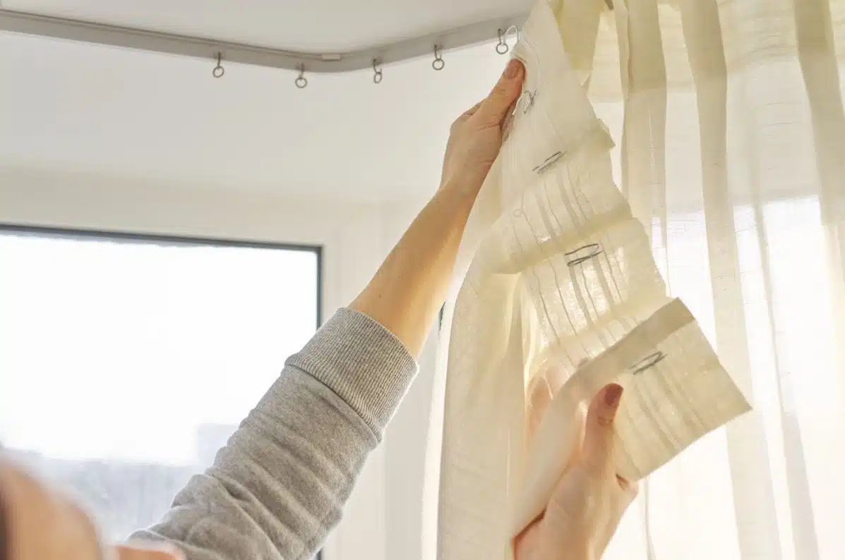 person unhooking white curtains from curtain rods