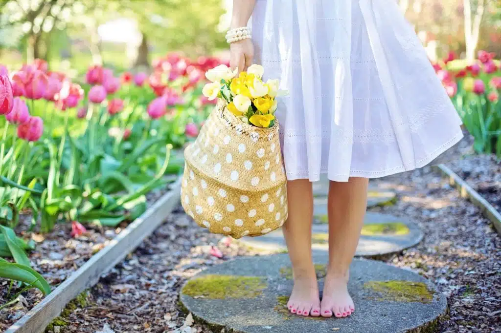 A lady standing barefoot with a basket of flowers on a sunny day.