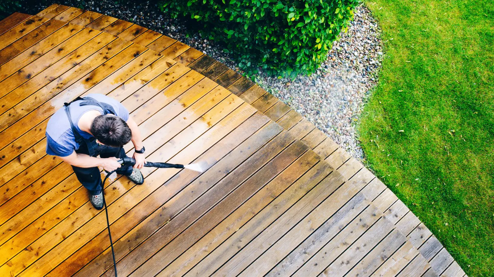 top view of a man in dark coloured overalls pressure washing a dirty patio