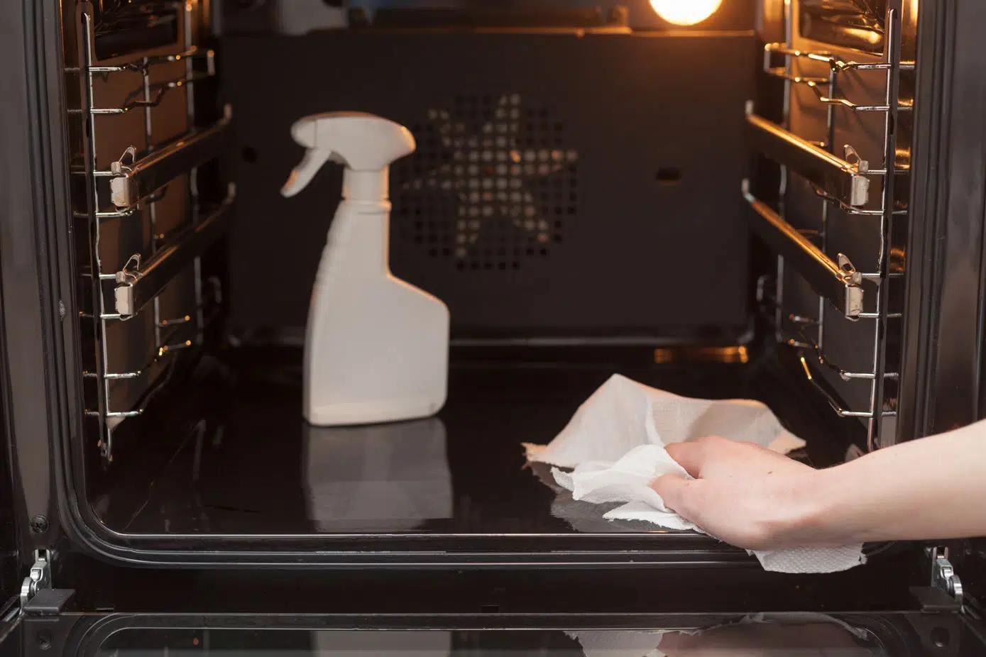 woman cleaning oven glass with a white spray bottle that is sitting on the inside of the oven