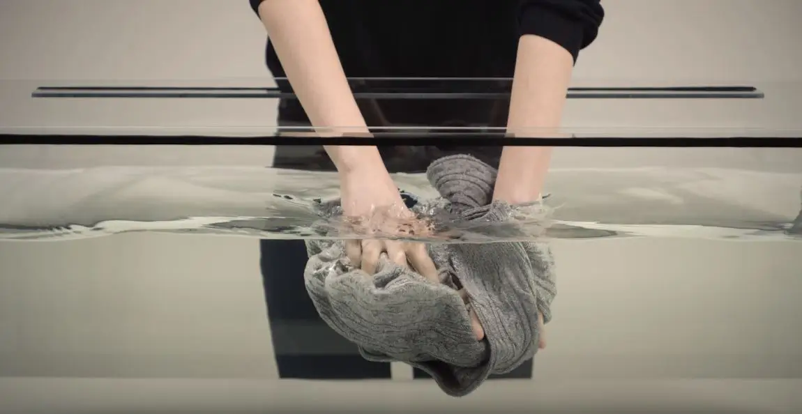 woman handwashing grey sweater in a large tub full of water