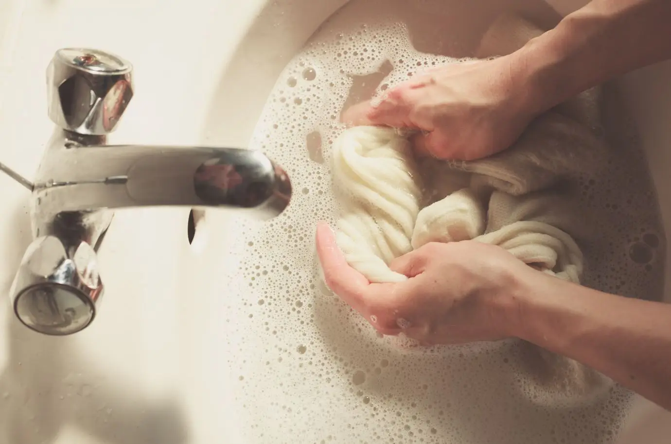 woman handwashing white jumper in bathroom sink