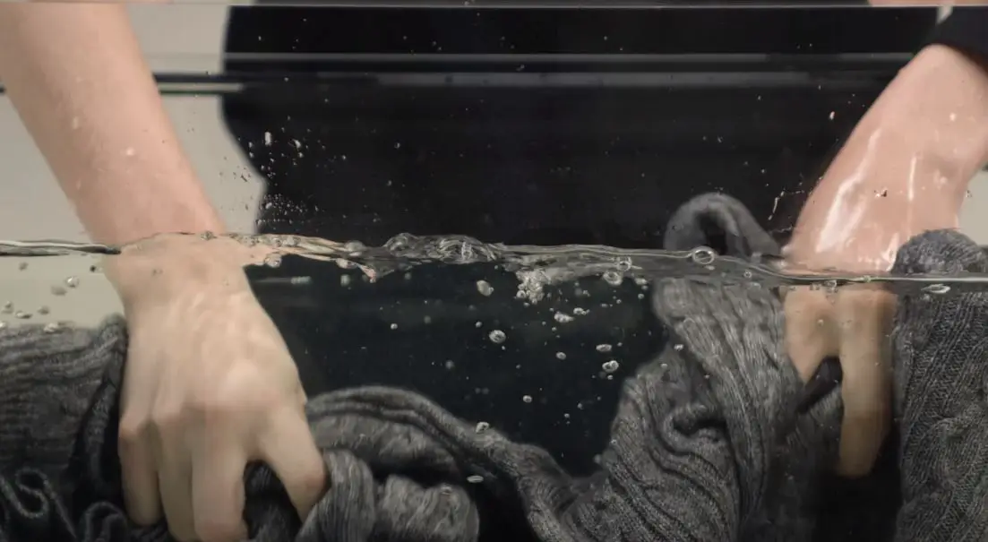 woman scrubbing grey sweater in large tub full of water